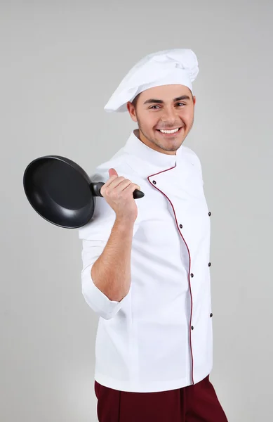 Chef profissional em uniforme branco e chapéu, segurando panela em suas mãos, em fundo cinza — Fotografia de Stock