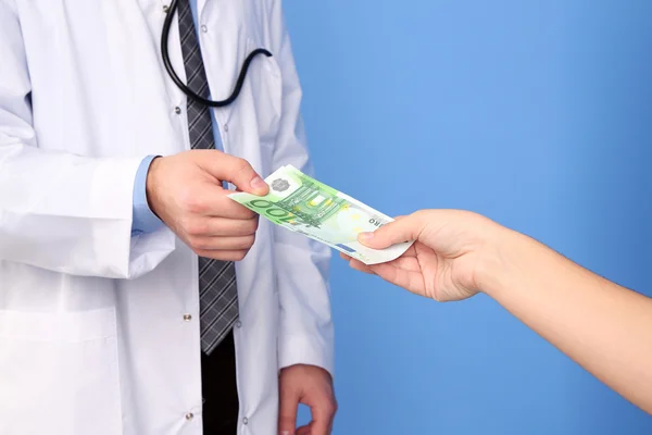 Αρσενικό γιατρός που λαμβάνουν χρήματα από ασθενή, σε μπλε φόντο — Zdjęcie stockowe