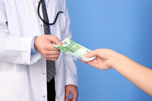 Male Doctor receiving money from patient, on blue background — Stock Photo, Image