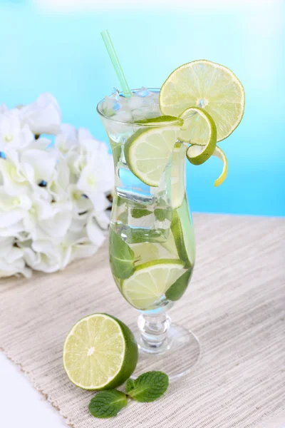 Bicchiere di cocktail con lime e menta sul tavolo su sfondo azzurro — Foto Stock