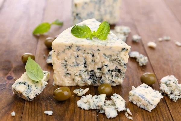 लाकडी टेबलवर ऑलिव्ह आणि बासिलसह स्वादिष्ट निळा चीज — स्टॉक फोटो, इमेज