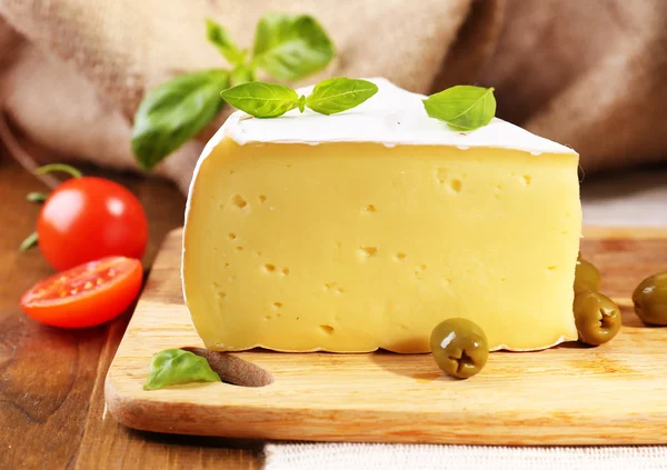 Smakelijke camembert kaas met olijven, tomaten en basilicum, op houten tafel — Stockfoto