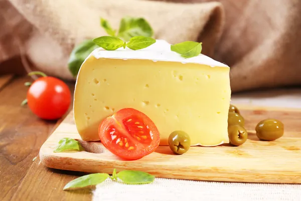 Tasty Camembert cheese with tomatoes, olives and basil, on wooden table — Stock Photo, Image