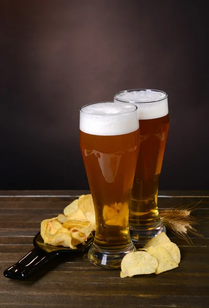 Vasos de cerveza con merienda en la mesa sobre fondo oscuro —  Fotos de Stock