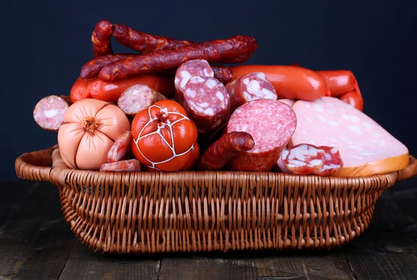 Много различных колбас в корзине на деревянном столе на черном фоне — стоковое фото