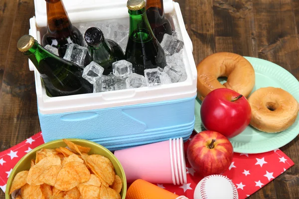 Ice chest full of drinks in bottles on color napkin, on wooden background — Stock Photo, Image