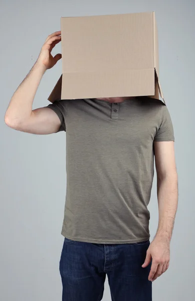 灰色の背景上の彼の頭の上の段ボール箱を持つ男 — ストック写真