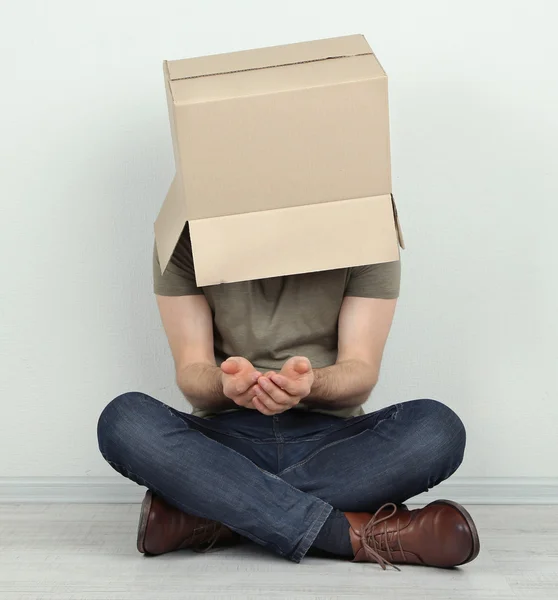 Hombre con caja de cartón en la cabeza sentado en el suelo cerca de la pared — Foto de Stock