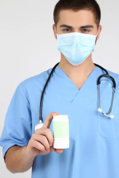 Jovem médico em máscara médica com pílulas, isolado em branco — Fotografia de Stock