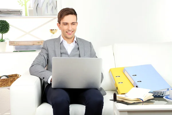 Jovem empresário usando laptop no sofá em casa — Fotografia de Stock
