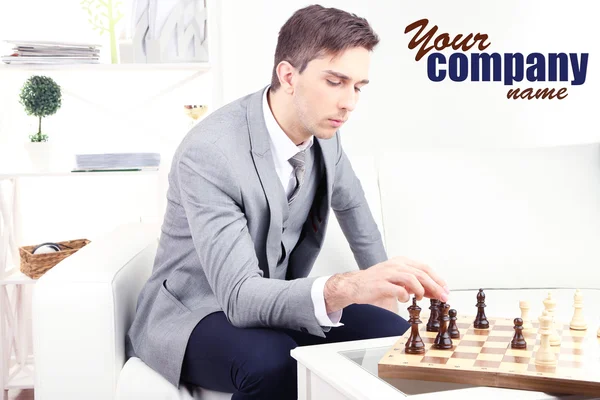Elegante giovane uomo d'affari seduto sul divano e giocare a scacchi, a casa — Foto Stock
