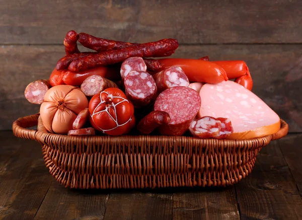 Beaucoup de différentes saucisses dans le panier sur une table en bois sur fond en bois — Photo