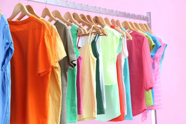 Different clothes on hangers, on pink background — Stock Photo, Image