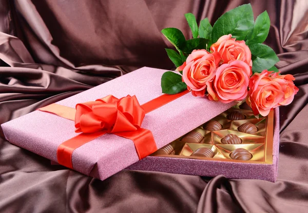 Delicious chocolates in box with flowers on brown background — Stock Photo, Image