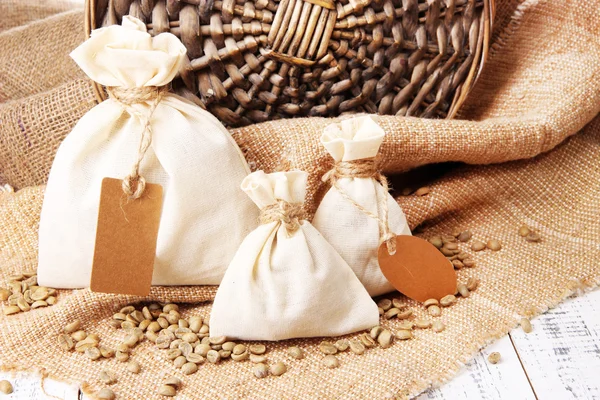 Zakken met koffiebonen op houten tafel, op rouwgewaad achtergrond — Stockfoto