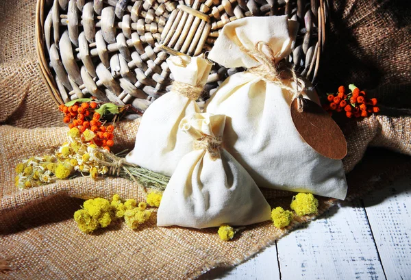 Sachet textile avec fleurs séchées, herbes et baies sur table en bois, sur fond de sac — Photo