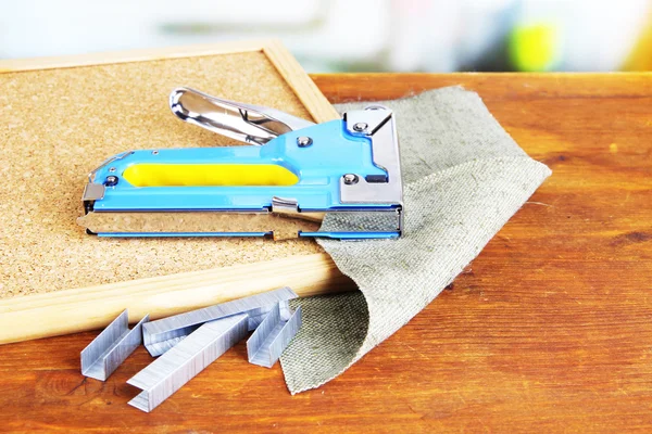 Grapadora de construcción con grapas y tablero de corcho en la mesa sobre fondo brillante —  Fotos de Stock