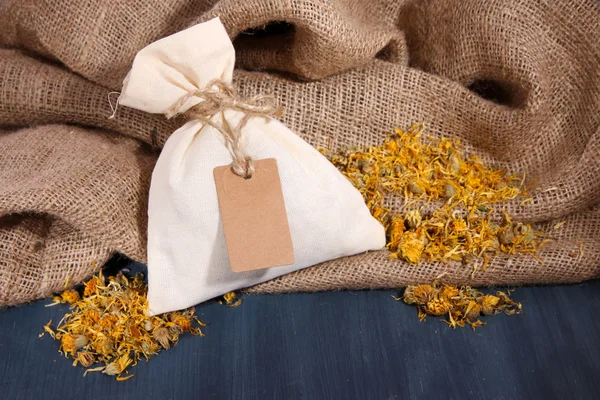 Textile sachet pouch with dried flowers on wooden table, on sackcloth background — Stock Photo, Image