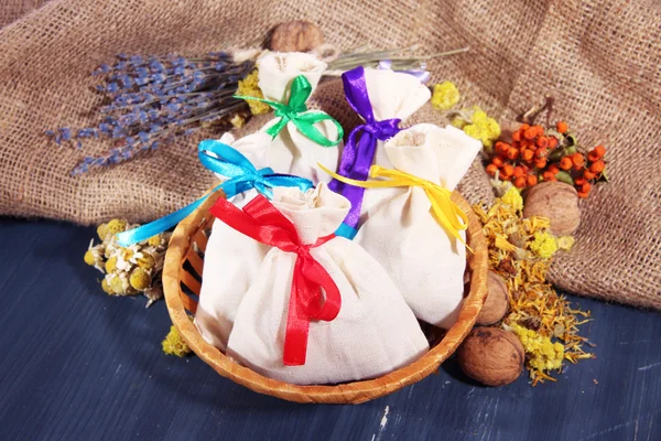 Textile sachet pouches with dried flowers, herbs and berries on wooden table, on sackcloth background — Stock Photo, Image