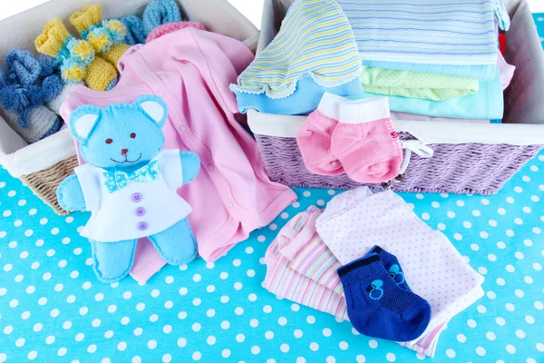 Mucchio di vestiti per bambini nel cestino, sul tavolo sullo sfondo di colore — Foto Stock