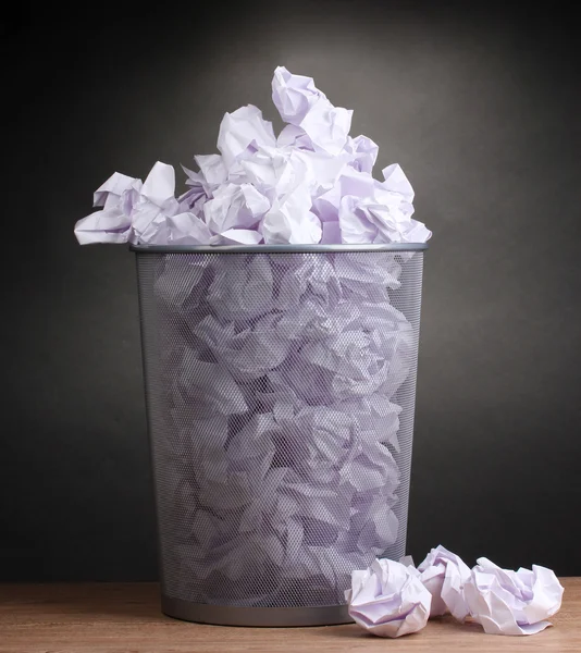 Metal trash bin from paper on wooden floor on gray background