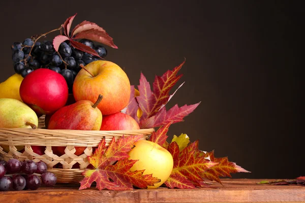 Beautiful autumn harvest in basket and leaves on brown background — Stock Photo, Image