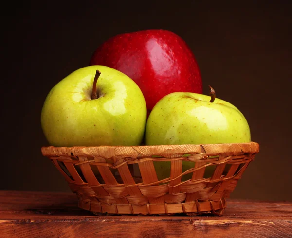 Juicy sweet apples in basket on wooden table on brown background — Stock Photo, Image