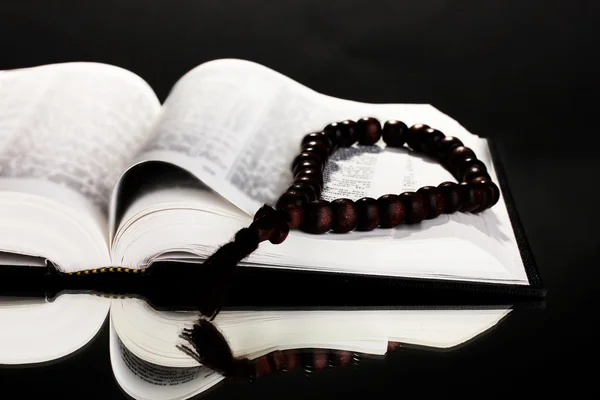 Biblia russa e rosário de madeira sobre fundo preto — Fotografia de Stock