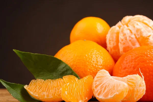 Tangerines with leaves on wooden table on brown background — Stock Photo, Image