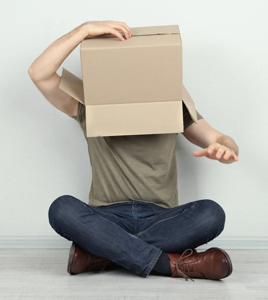 Homme avec boîte en carton sur la tête assis sur le sol près du mur — Photo