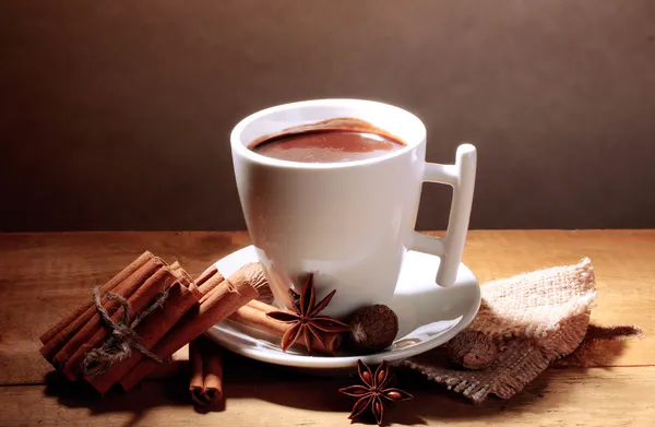 Tazza di cioccolata calda, bastoncini di cannella, noci e cioccolato su tavolo di legno su sfondo marrone — Foto Stock