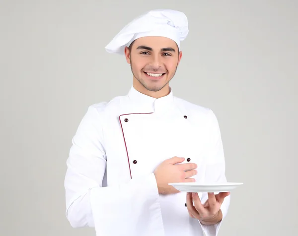 Professionele chef-kok in het witte uniform en hoed, op grijze achtergrond — Stockfoto