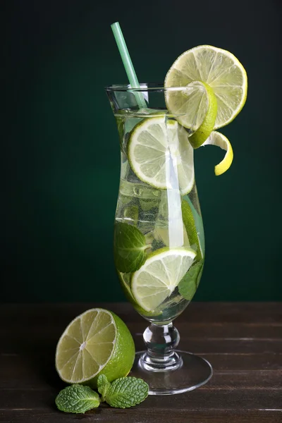 Cocktailglas mit Limette und Minze auf Tisch auf dunkelgrünem Hintergrund — Stockfoto