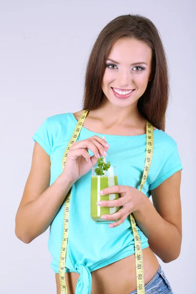 Menina bonita com suco fresco e fita métrica no fundo cinza — Fotografia de Stock