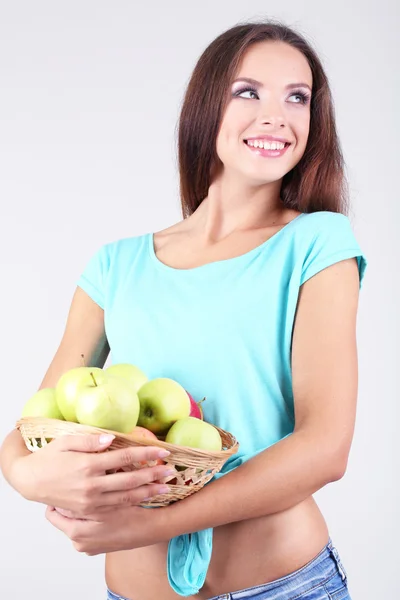 Belle jeune femme avec panier de pommes vertes sur fond gris — Photo