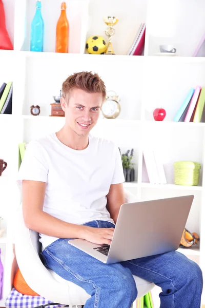 Ung man avkopplande med laptop, på hem inredning bakgrund — Stockfoto