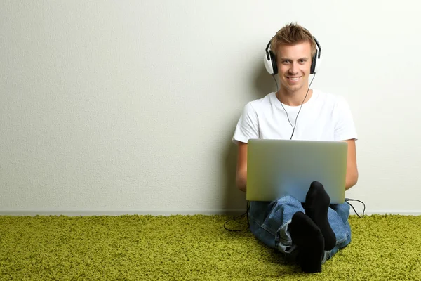 Jonge man ontspannen op tapijt en luisteren naar muziek, op grijze muur achtergrond — Stockfoto