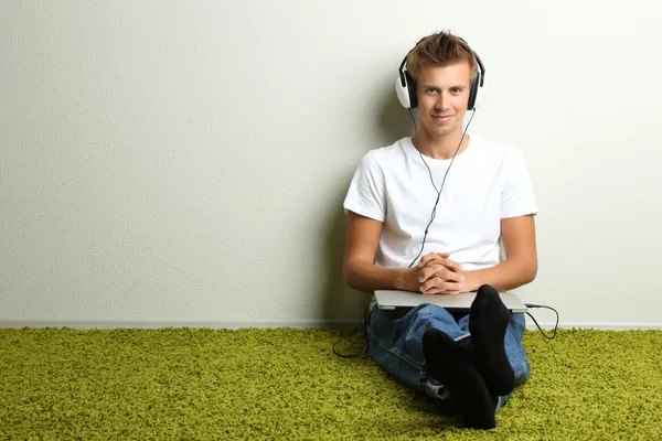 Hombre joven relajándose en la alfombra y escuchando música, sobre fondo gris de la pared —  Fotos de Stock