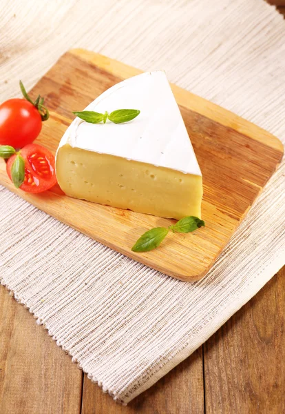 Tasty Camembert cheese with tomato and basil, on wooden table — Stock Photo, Image