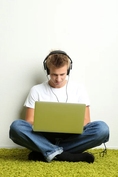 Junger Mann entspannt auf Teppich und hört Musik, auf grauem Wandhintergrund — Stockfoto