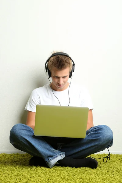 Hombre joven relajándose en la alfombra y escuchando música, sobre fondo gris de la pared — Foto de Stock