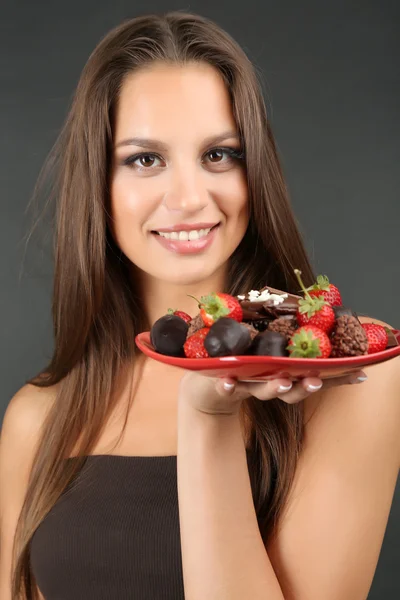 Портрет красивой молодой девушки с шоколадными конфетами на тарелке на сером фоне — стоковое фото