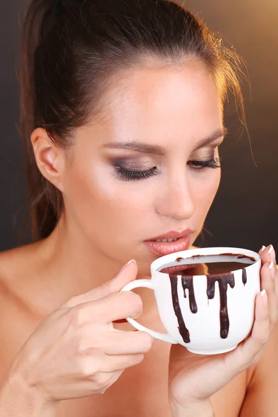 Retrato de hermosa joven con taza de chocolate caliente sobre fondo marrón — Foto de Stock