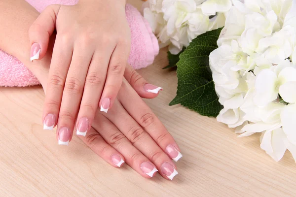 Belas mãos de mulher com manicure francês e flores em fundo de madeira — Fotografia de Stock