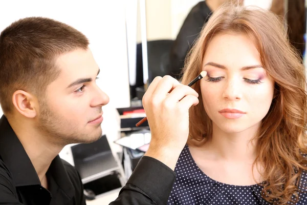 Young guy stylist doing makeup beautiful woman in beauty salon — Stock Photo, Image