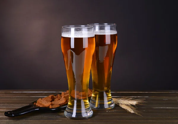Copos de cerveja com lanche na mesa no fundo escuro — Fotografia de Stock