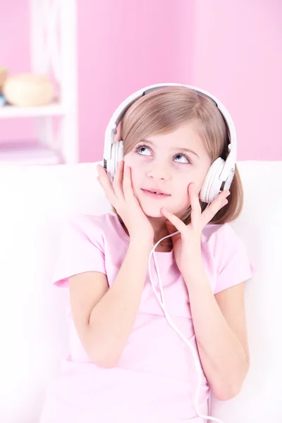 Liten flicka sitter på soffan och lyssnar musik i rum — Stockfoto