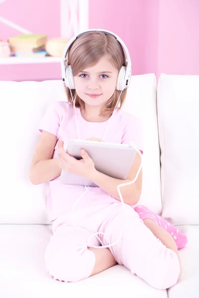 Küçük kız kanepede oturan ve odada müzik dinleme — Stok fotoğraf