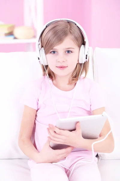 Little girl sitting on sofa and listening music in room — Stock Photo, Image