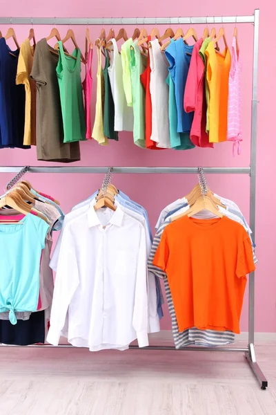 Different clothes on hangers, on pink background — Stock Photo, Image